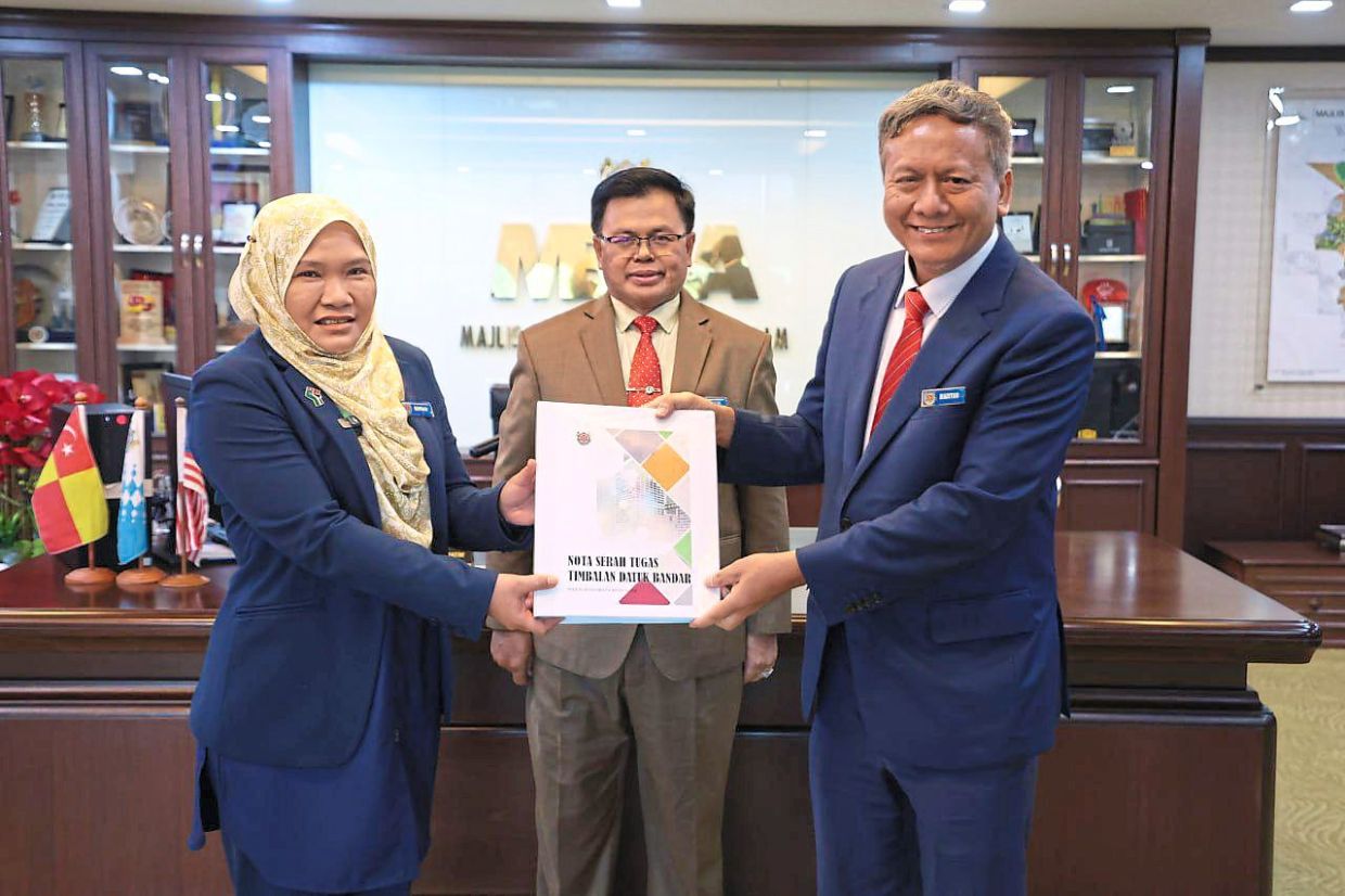 Safriah (left) receiving a manual on her role as Shah Alam deputy mayor from Madiyan (right) while Mohd Fauzi looks on.