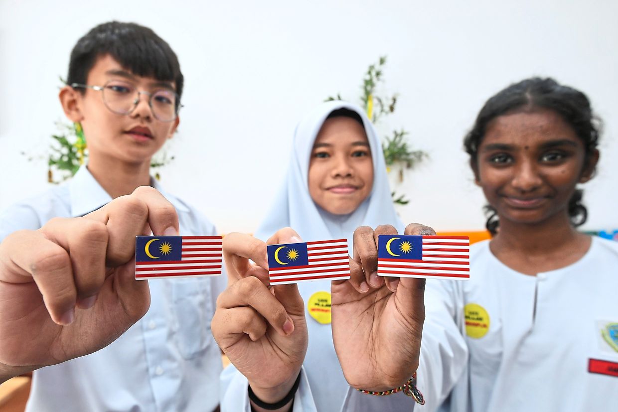 (From left) Gooi You He, Airin Husna and Amrita Shri showing their Jalur Gemilang badges before pinning them on their school uniforms outside a secondary school.
