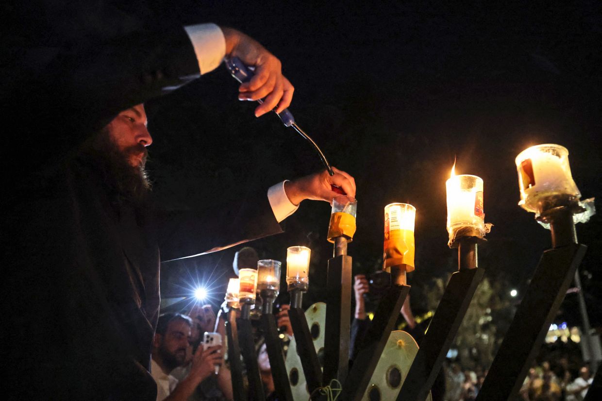 4. The seventh candle on a menorah is lit for the Jewish festival of Hanukkah as mourners gather next to floral tributes laid out in memory of the victims in Sydney. — AFP