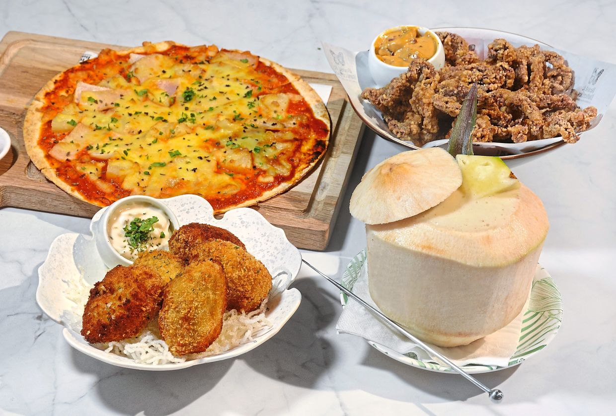 The Pina Colada, served in a coconut, alongside (clockwise from bottom left) Tuna and Egg Croquettes, Hawaiian Pizza and Crispy Squid.