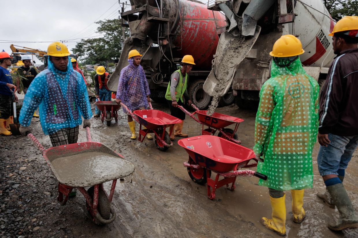 Workers carry concrete in wheelbarrows during the construction of temporary housing units built by Danantara, an Indonesian state-owned investment agency, in Aceh Tamiang, Aceh province. -- Photo by ADITYA AJI / AFP