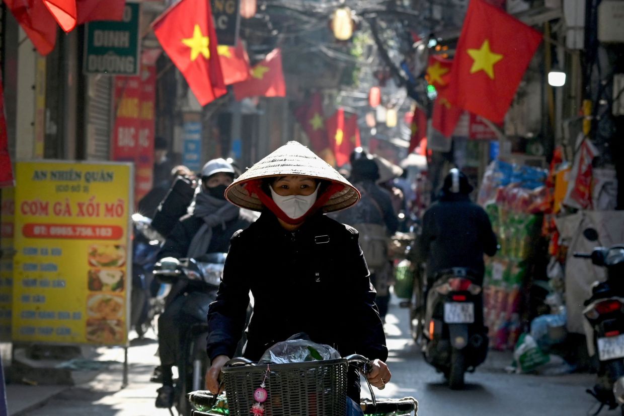 A street vendor rides a bicycle along a street under Vietnamese flags in Hanoi, -- Photo by Nhac NGUYEN / AFP