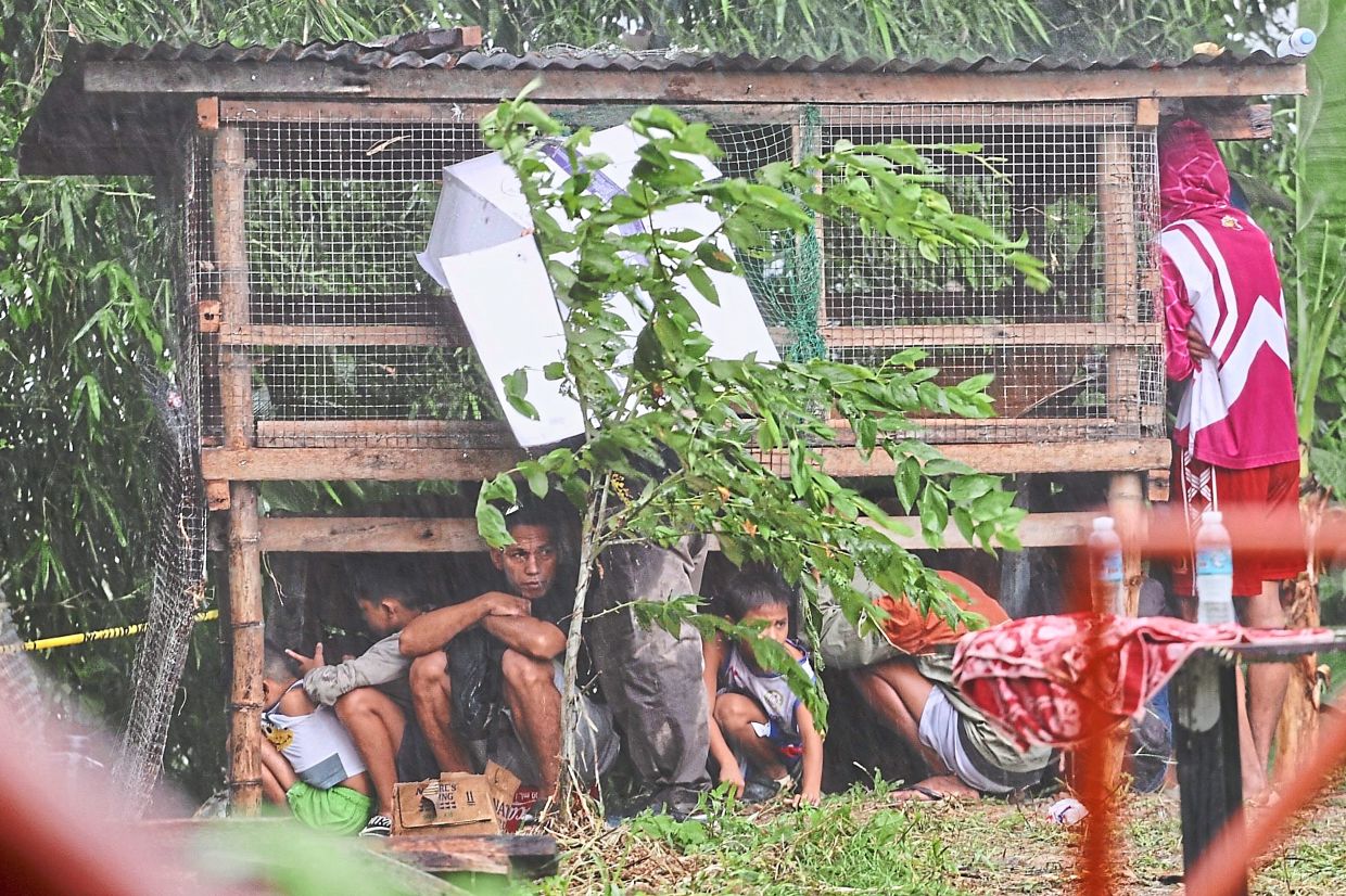 Tense situation: Family members and relatives of victims taking shelter under a chicken coop while waiting for news as rescue operations continue at the collapsed waste segregation facility in Binaliw. — AP