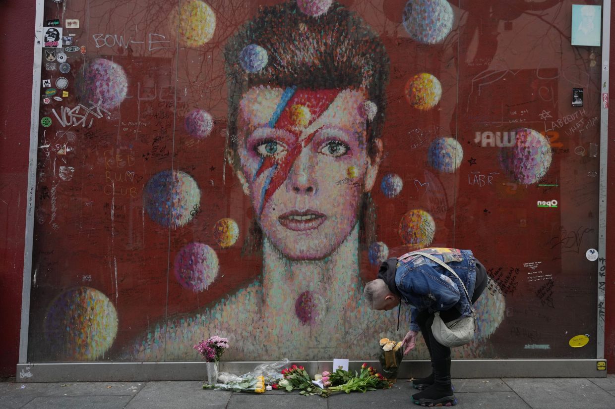 A Bowie fan places a flower bouquet in front of a mural in London to commemorate the 10th anniversary of his death on Jan 10. Photo: AP 