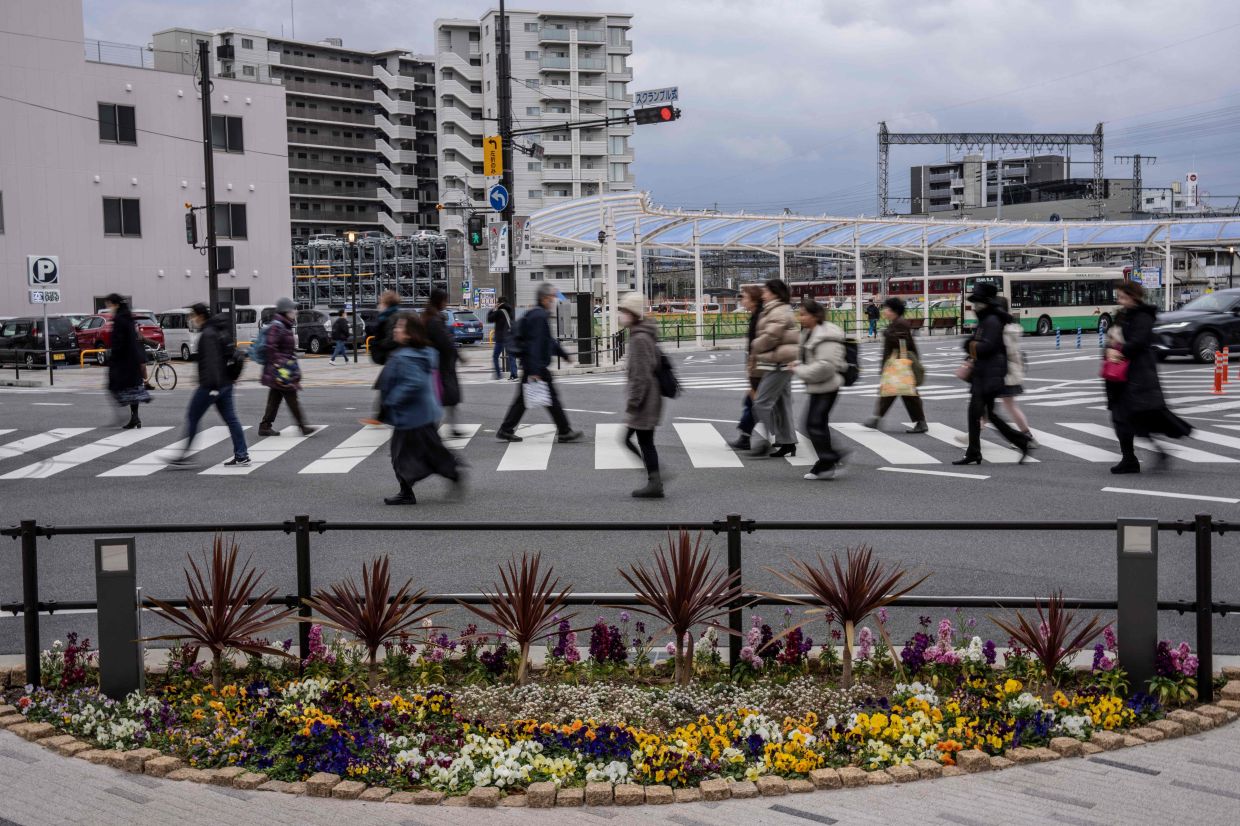 People walk past a flower bed set up as a memorial at the intersection in front of Kintetsu Yamato-Saidaiji Station, where Japan's former prime minister Shinzo Abe was fatally shot while delivering an election campaign speech, in Nara on Tuesday, January 13, 2026. -- Photo by Yuichi YAMAZAKI / AFP