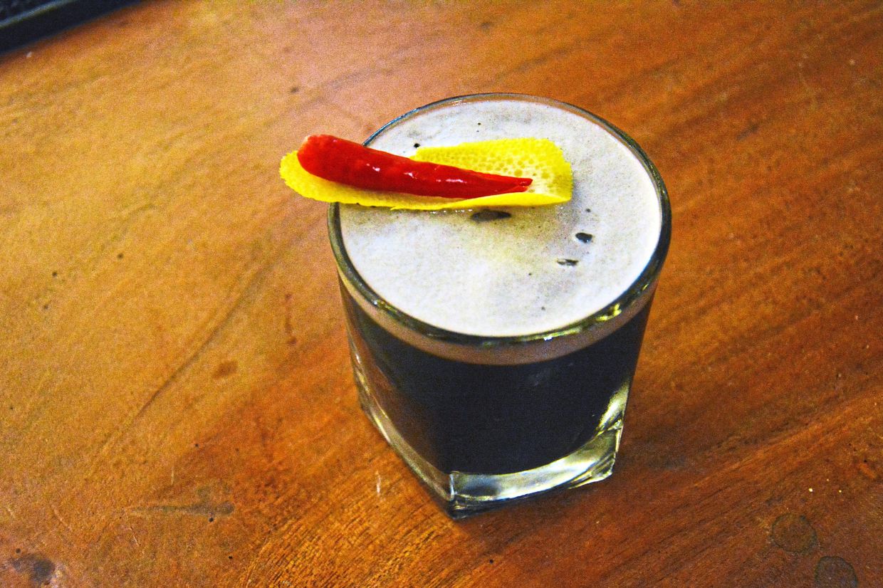 The Devil’s Delight is a striking black cocktail made with activated charcoal, lime, spicy homemade syrup, and egg white, topped with a fiery red bird’s eye chilli. — Photos: JAROD LIM/The Star