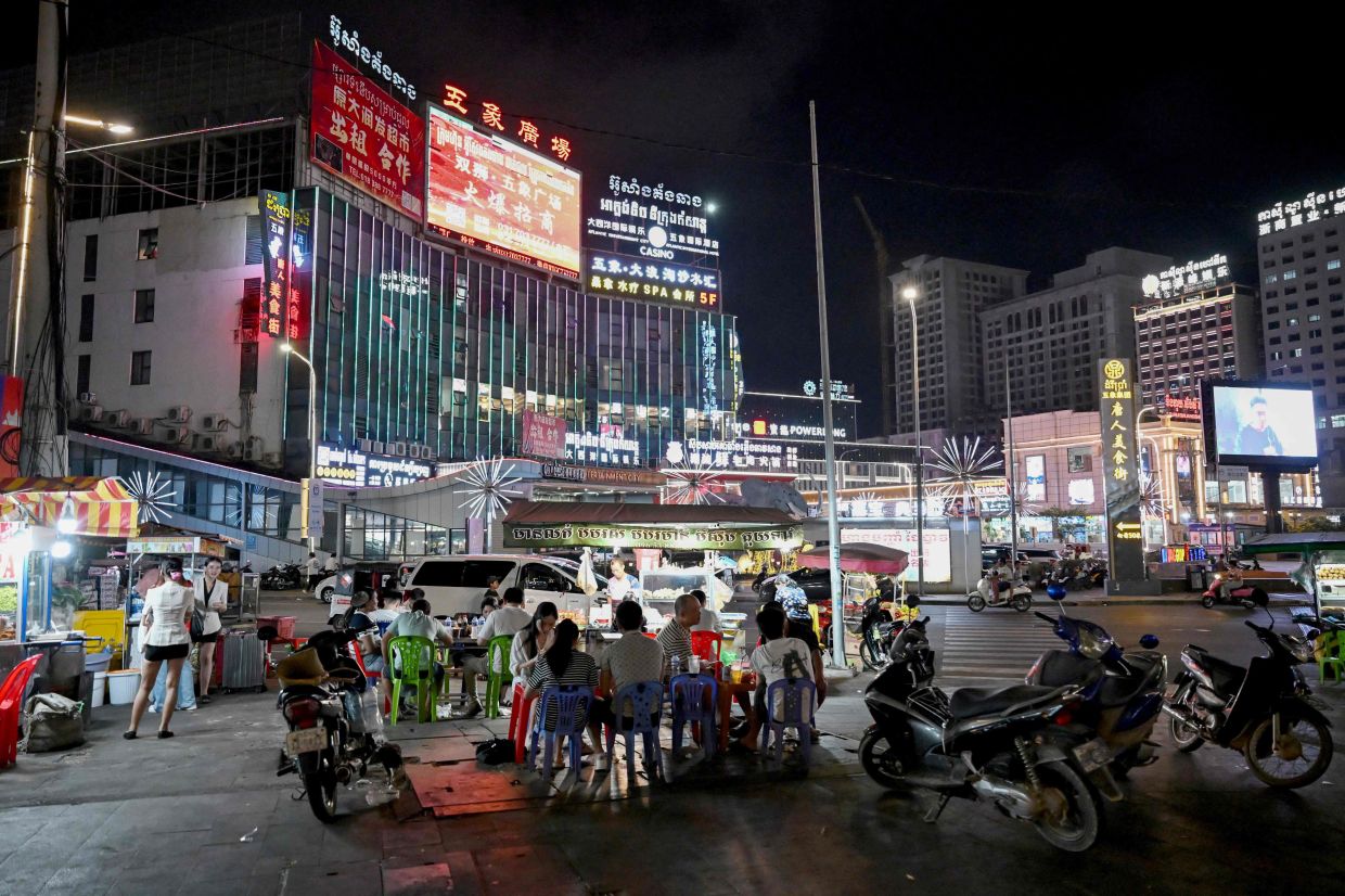 People eat next to street food stalls in Sihanoukville, Cambodia. -- Photo by TANG CHHIN Sothy / AFP