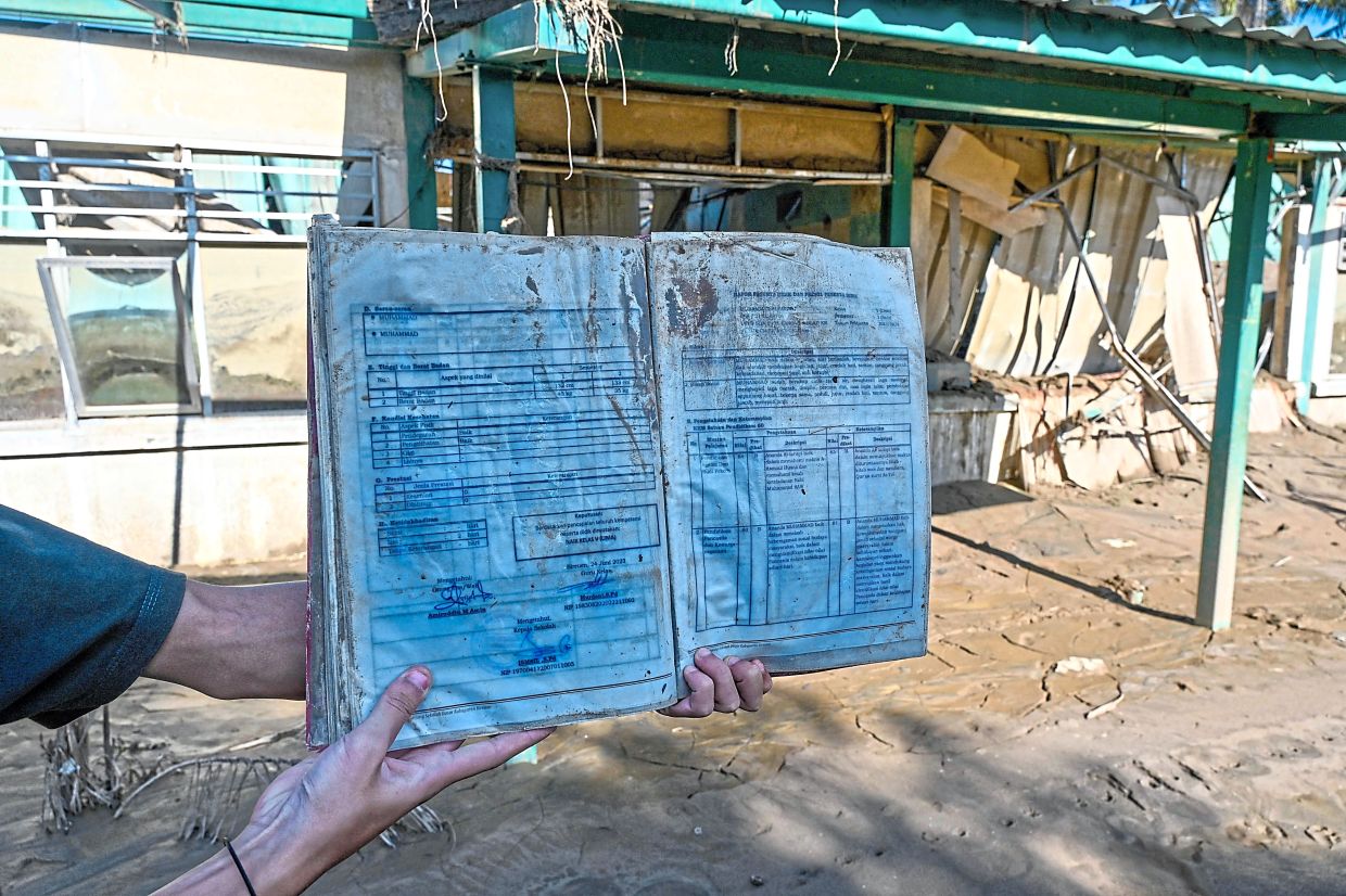 A flood survivor showing a child’s water-damaged school book in Indonesia. Aid to rebuild lives is needed now, not five years down the road when developed countries finally agree on legal terms. — AFP
