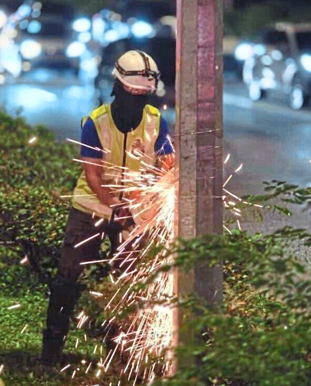 A DBKL worker cutting away coils of steel wires used to fix illegal banners on a lamp post.