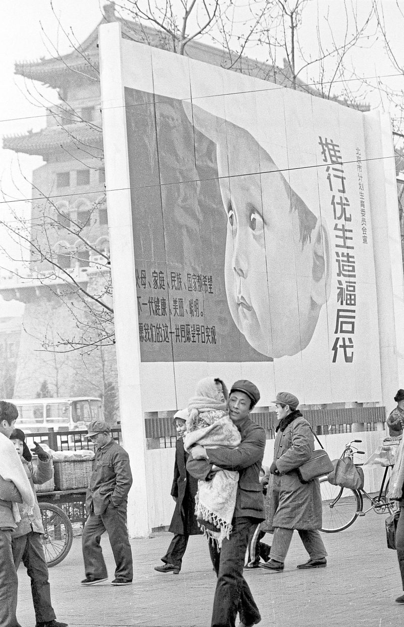 Managing the masses: A file photo of a man holding a child as he walks past a billboard with the words ‘practise birth control to benefit the next generation’, in the Front Gate area in Peking, on Feb 22, 1983. — AP