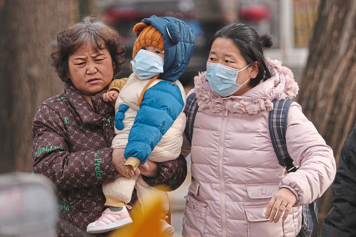 Women carrying a toddler across a street in Beijing. Plans for the nation’s next five-year plan for development include an aim to ‘encourage ­positive views on marriage and childbearing’. — AFP/AP