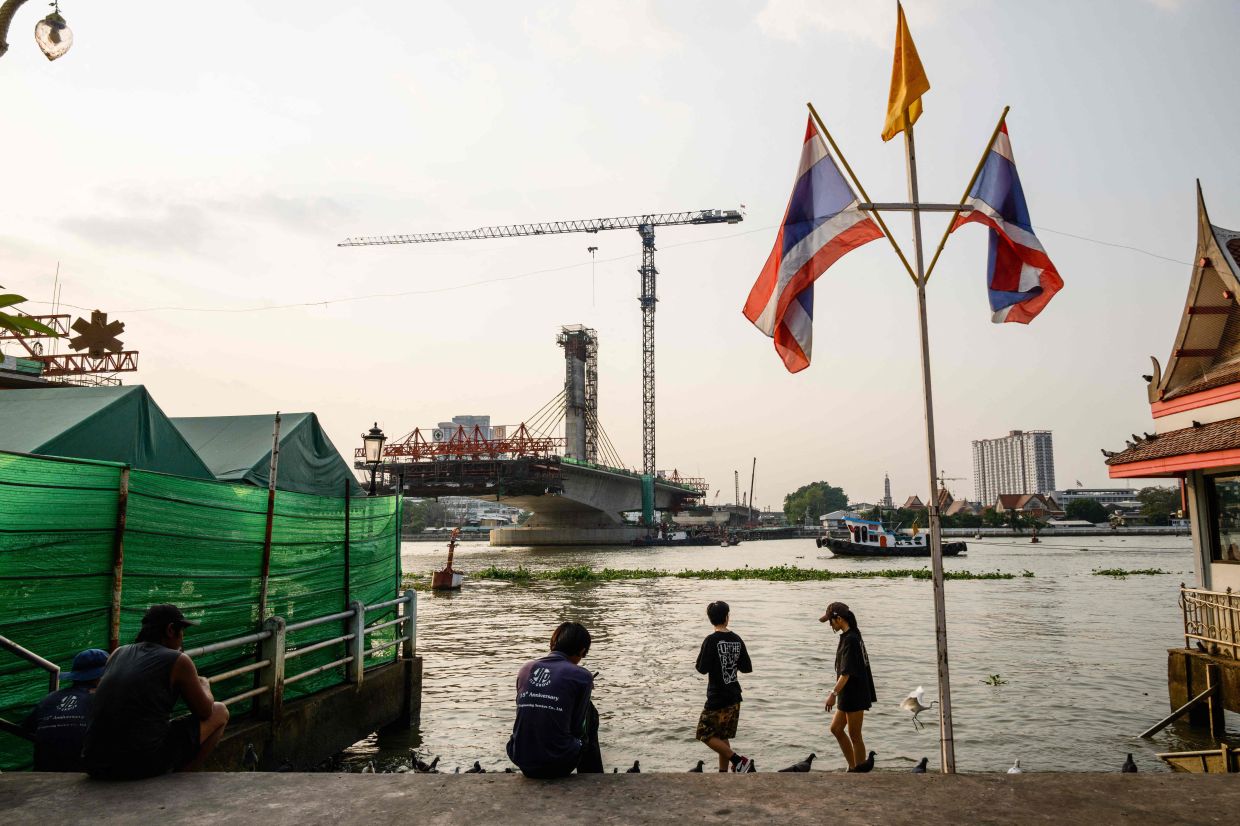 People relax near the site of a bridge (back centre) being constructed over the Chao Phraya River in Bangkok by the construction firm Italian-Thai Development (ITD).-- Photo by Anthony WALLACE / AFP