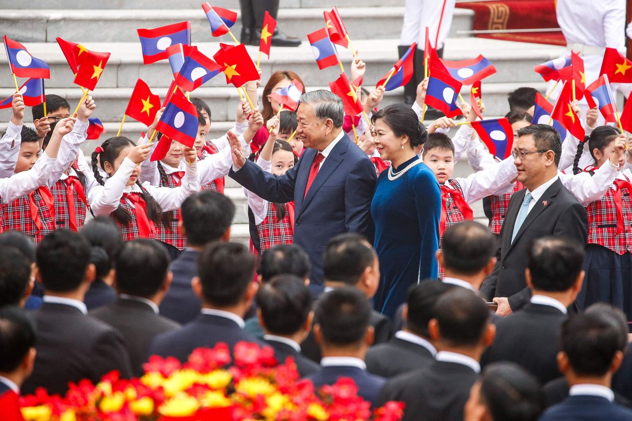Vietnam's Communist Party General Secretary To Lam (centre) and his wife Ngo Phuong Ly (C-R) wave to children ahead of a welcoming ceremony at the presidential palace in Hanoi on Monday, January 26, 2026. -- Photo by LUONG THAI LINH / POOL / AFP