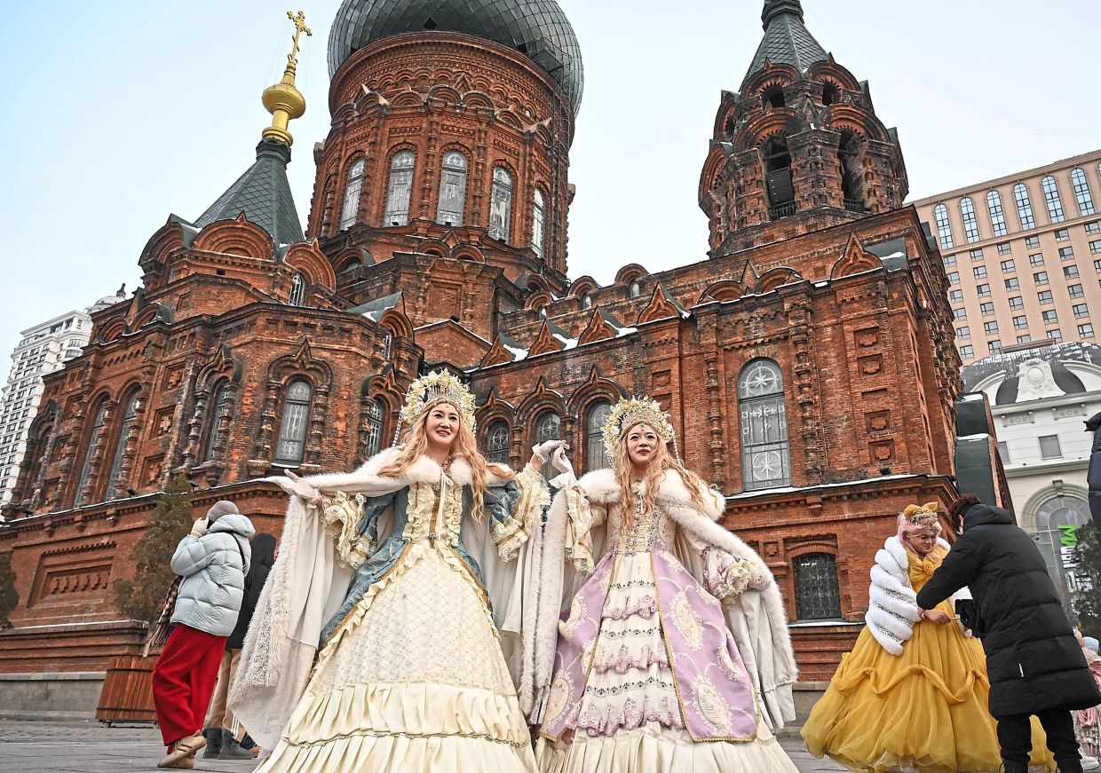 7. People in costumes posing for photographs outside Saint Sophia Cathedral in Harbin during the festival. — AFP