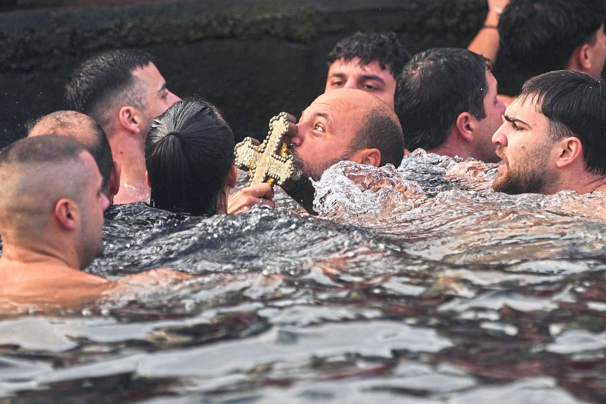 2. Greek Orthodox faithful kissing a wooden cross after it is retrieved from the Golden Horn during theepiphany ceremony in Istanbul, Turkiye. — AP