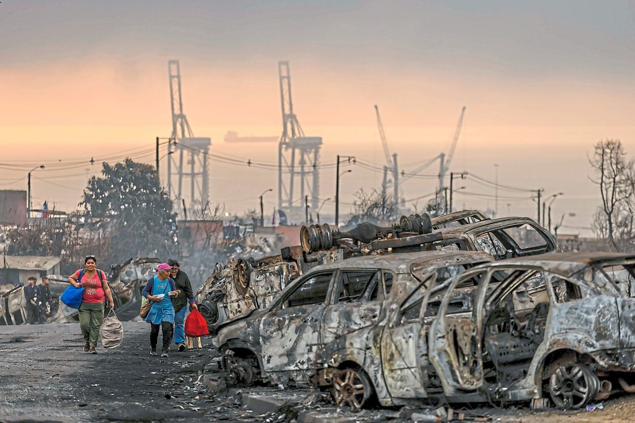 3. Residents transporting food to wildfire victims pass by charred vehicles in Lirquen. — AP