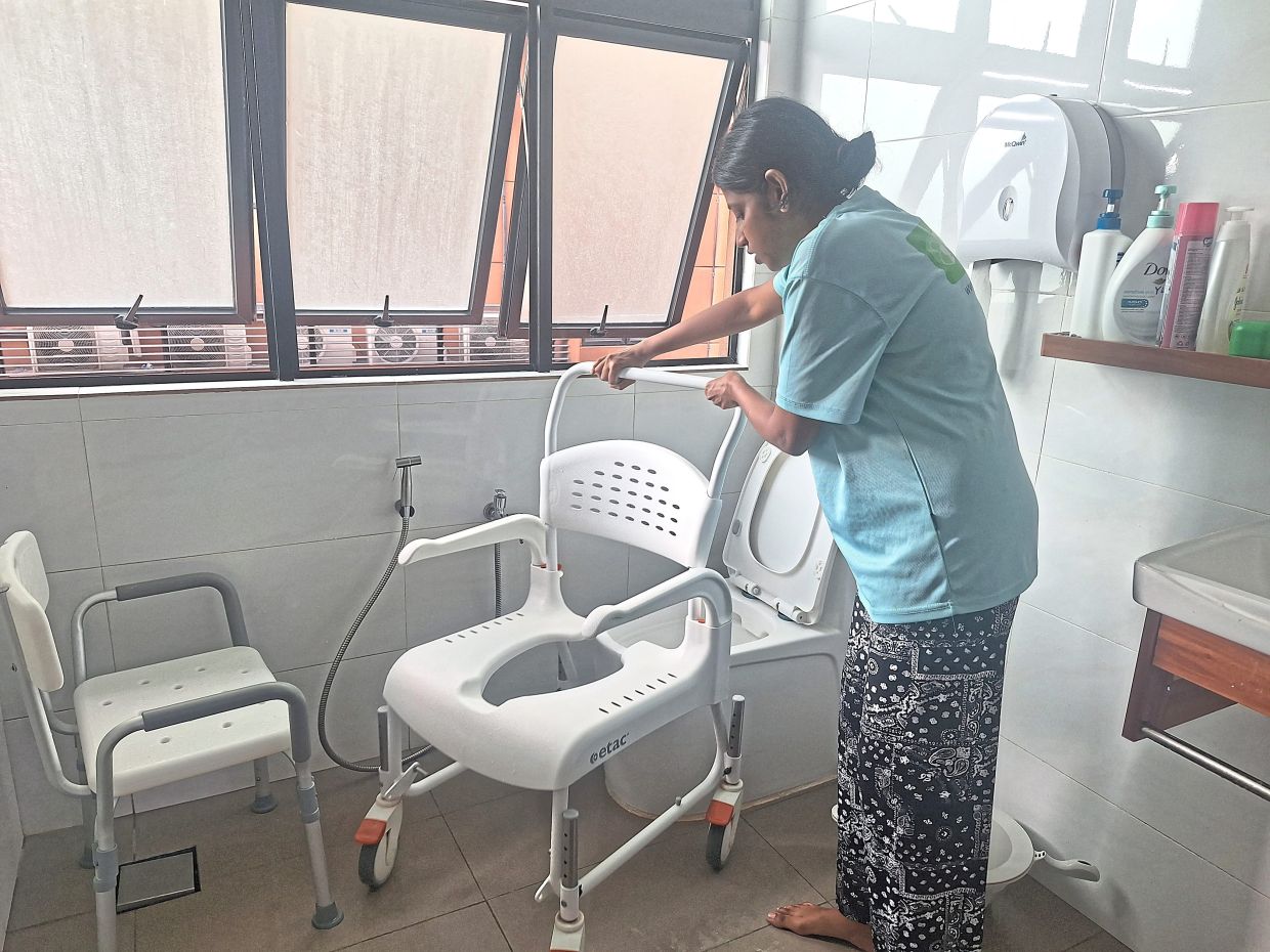 A care centre worker at an integrated healthcare hub in Subang Jaya shows how a commode is fixed to a toilet for elderly residents.