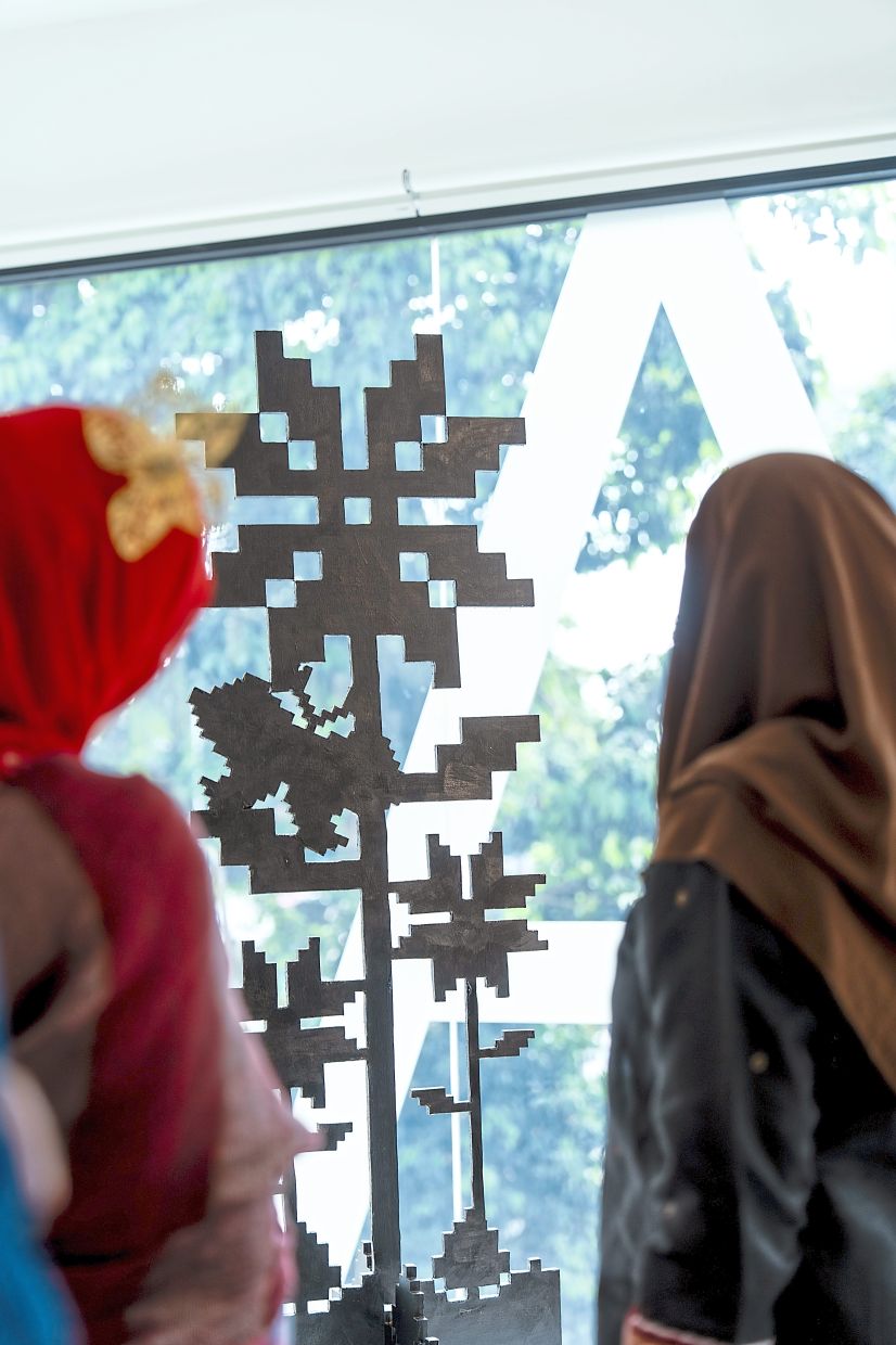 Visitors admire 'Harmonika', an acrylic-on-wood work in which Faizal weaves together motifs of bunga bintang, bunga pucuk and butterflies. Photo: Faizal Sidik