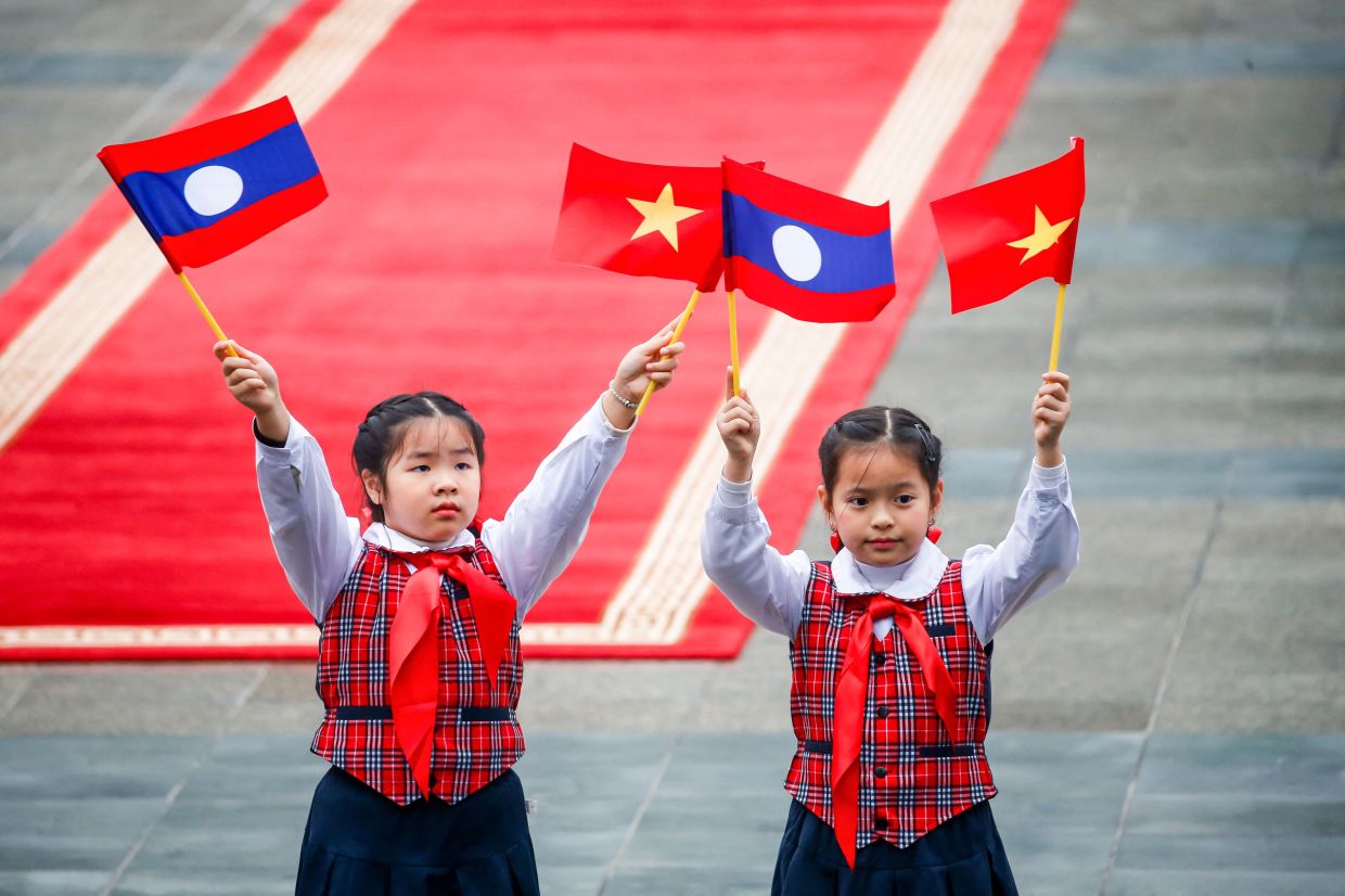 Children wave flags of Vietnam and Laos ahead of a welcoming ceremony at the presidential palace in Hanoi. - Photo by LUONG THAI LINH / AFP