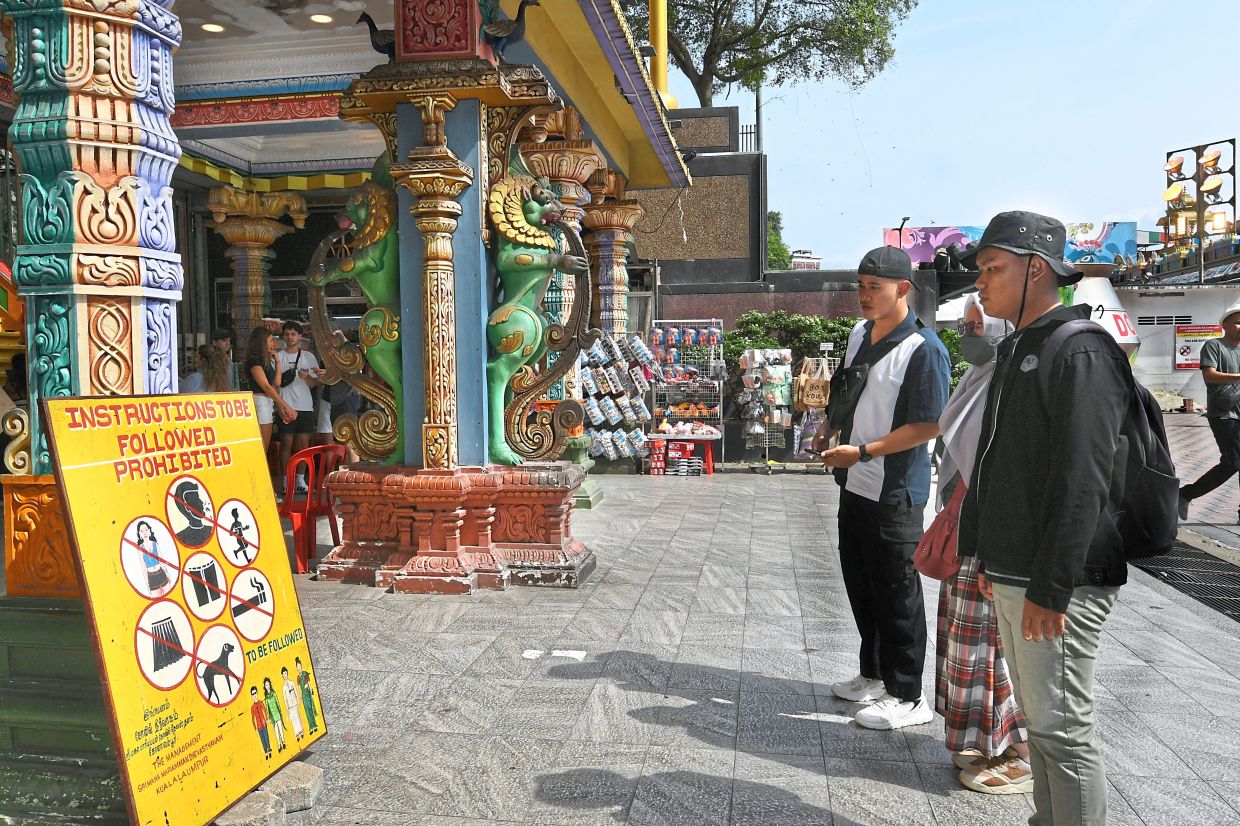 Batu Caves visitors looking at a sign on temple rules.
