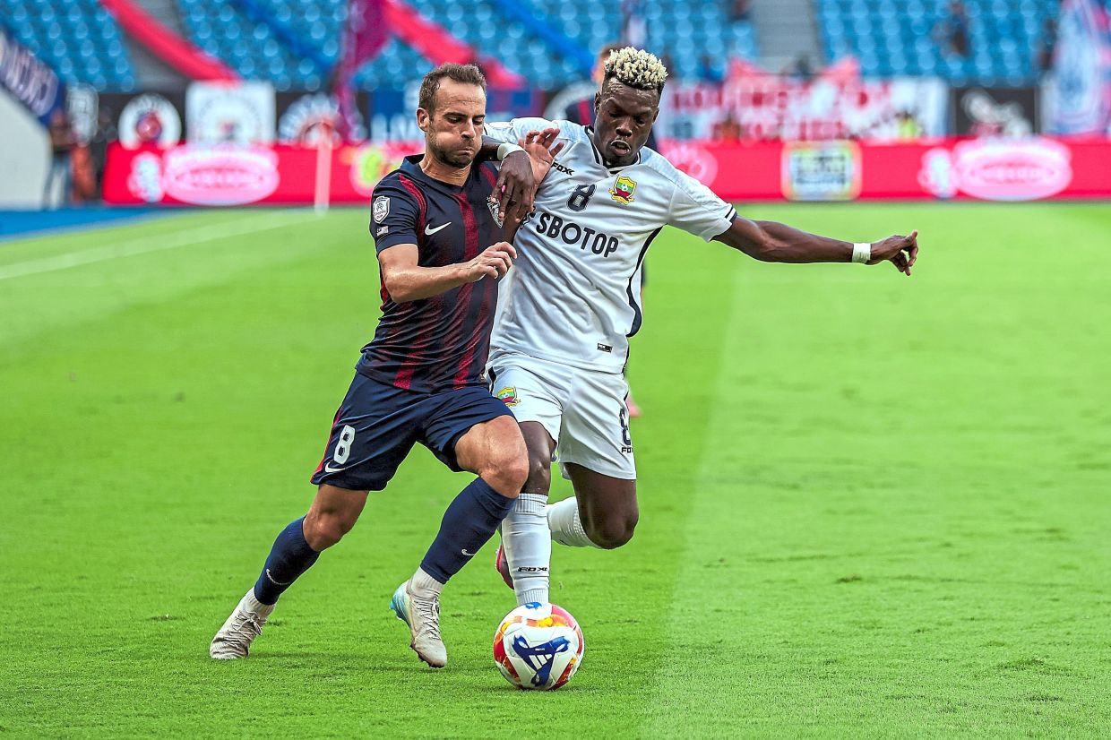 Move it: JDT’s Hector Hevel (left) gets a tight marking by Shan United’s Mark Sekyi. — Bernama 