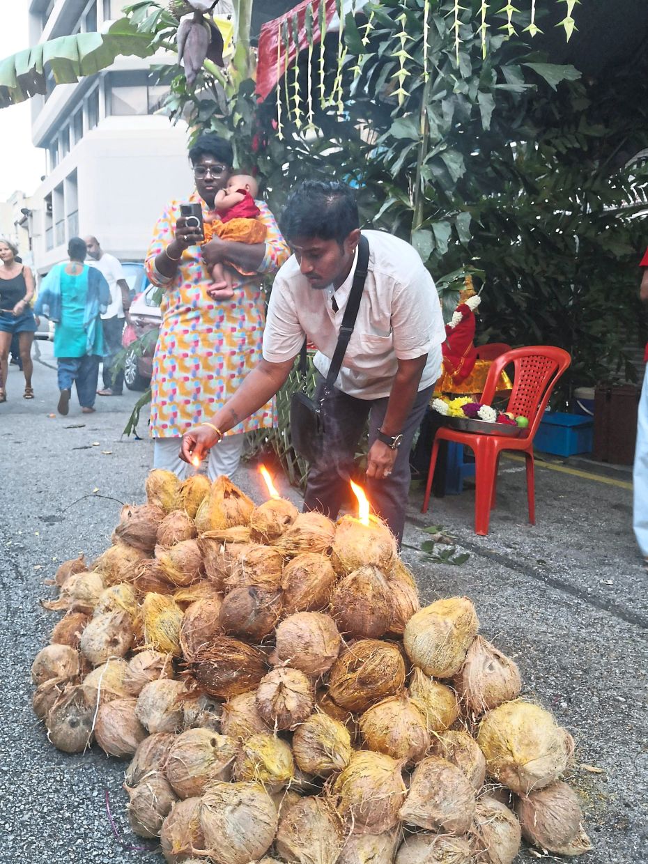 Devotees prepare coconut offerings along the procession route.