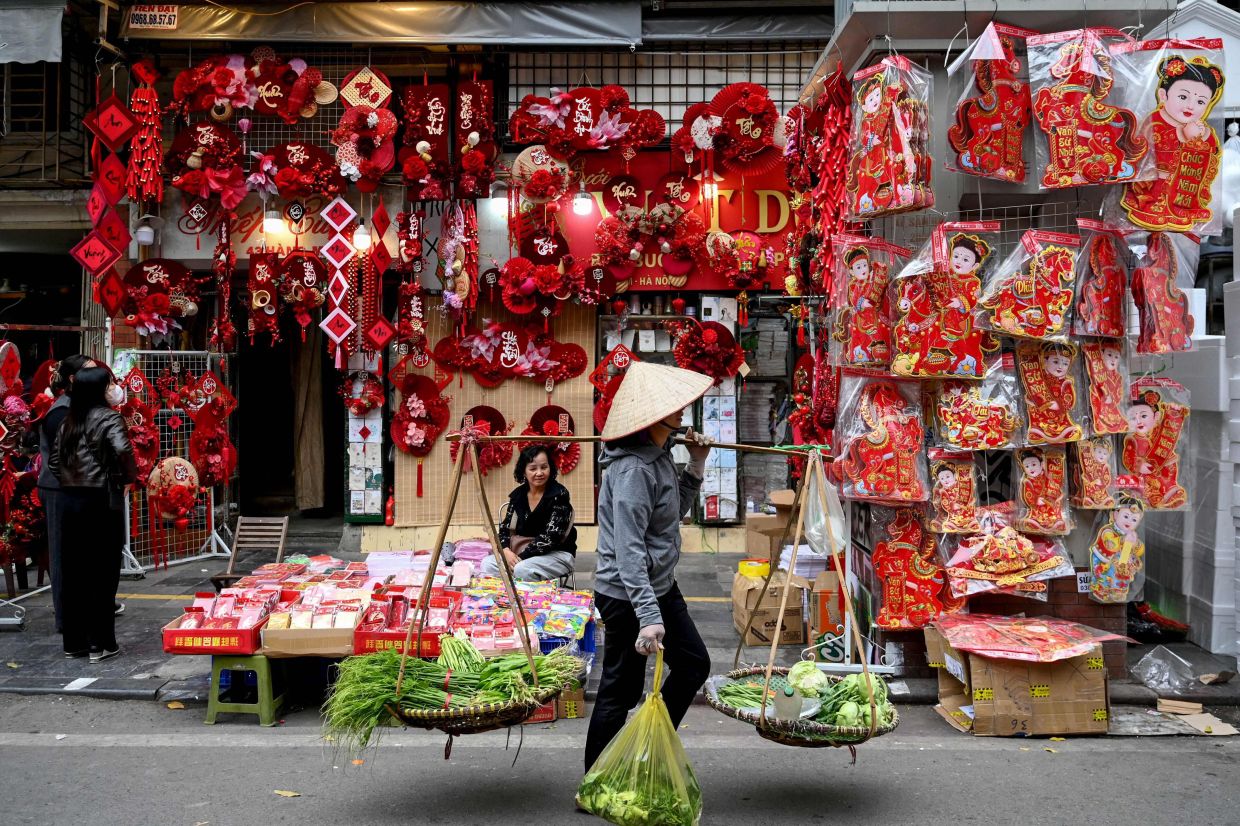 A street vendor walking past a shop selling decorations ahead of the Lunar New Year, known in Vietnam as Tet, in Hanoi on Feb 4, 2026. - AFP
