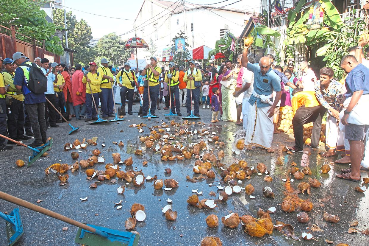 People smashing coconuts along the procession route during Thaipusam in Penang.