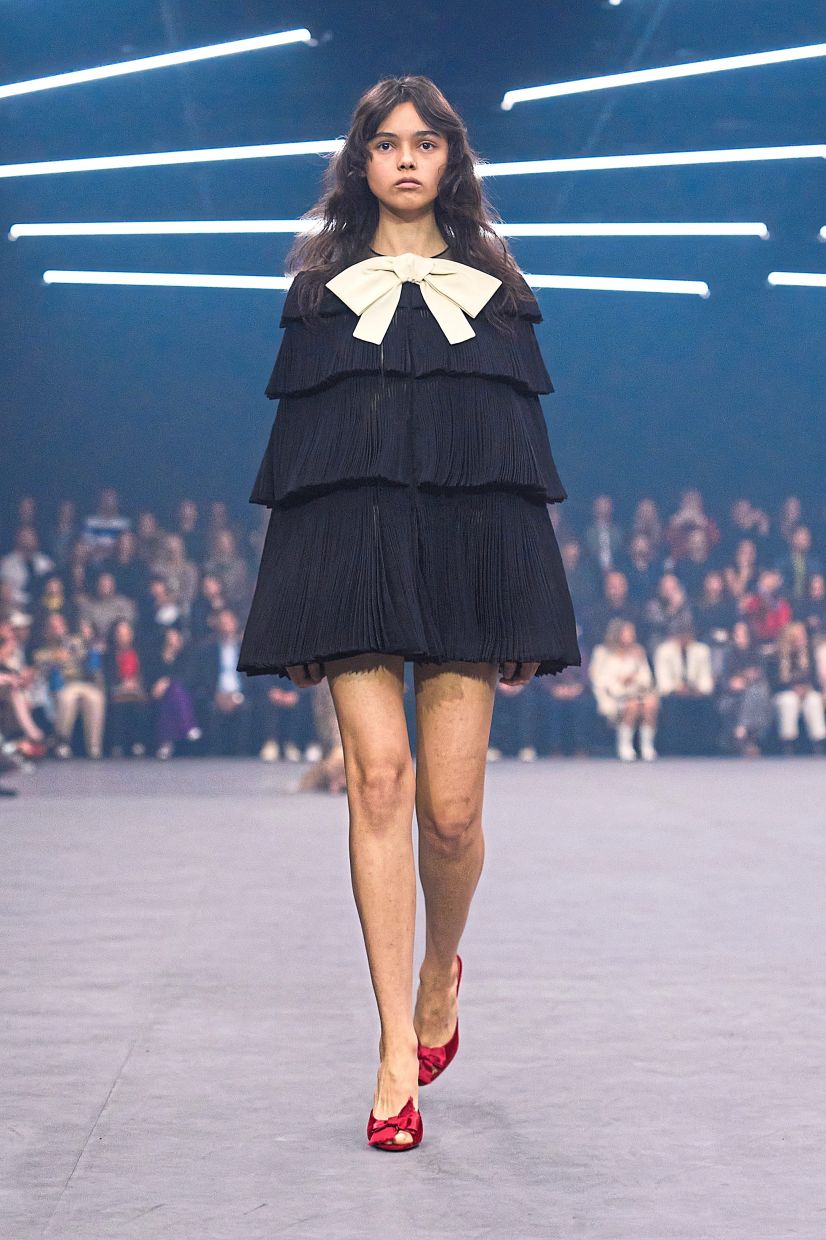An oversized white bow injects playful contrast into this black pleated number, while red beribboned shoes deliver a bold splash of colour. Photo: Valentino