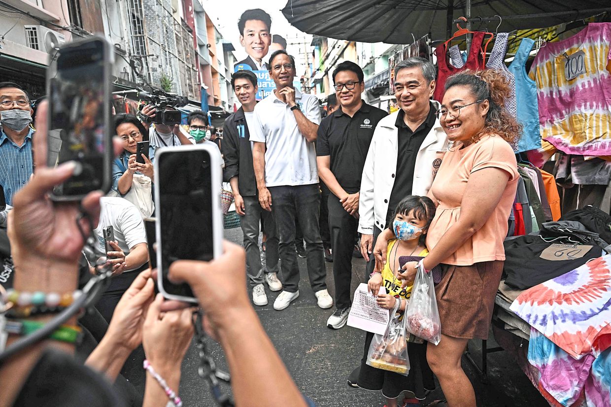 Meeting the people: Abhisit (second from right) taking pictures with people while campaigning at a Bangkok market. — AFP