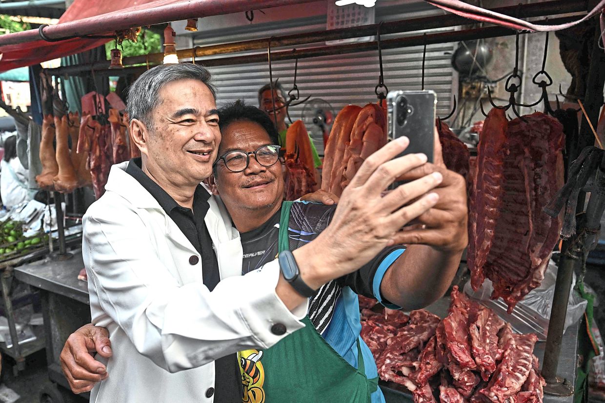 Abhisit taking a selfie with a market vendor. — AFP