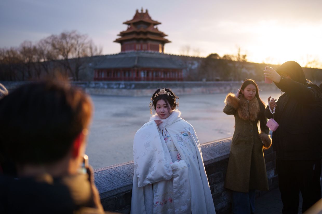 Tourists photograph a woman wearing traditional Chinese attire near the Forbidden City in Beijing, China, Friday, Feb. 6, 2026. -- AP Photo/Vincent Thian