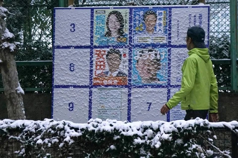 A man walks past a board displaying posters of candidates for the Lower House election along the street amidst the falling snow in Tokyo, on Feb 8. - Photo: AFP