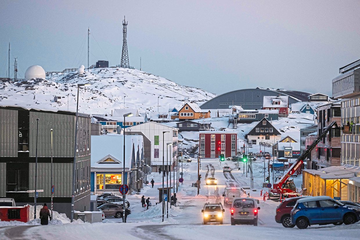 Cars drive along a snow covered street in downtown Nuuk. — AFP