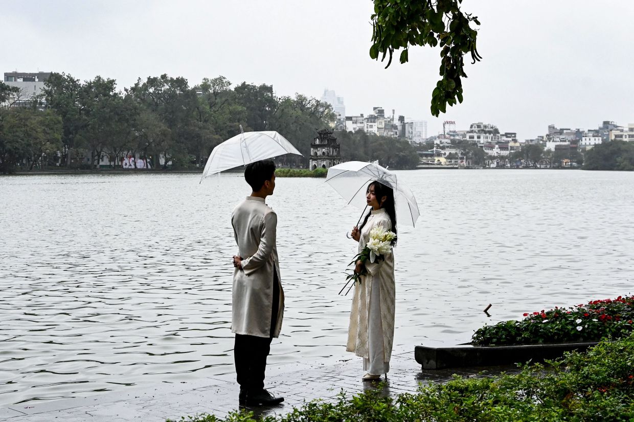 A couple holding umbrellas poses for photos at Hoan Kiem Lake in Hanoi on Monday, February 9, 2026. -- Photo by Nhac NGUYEN / AFP