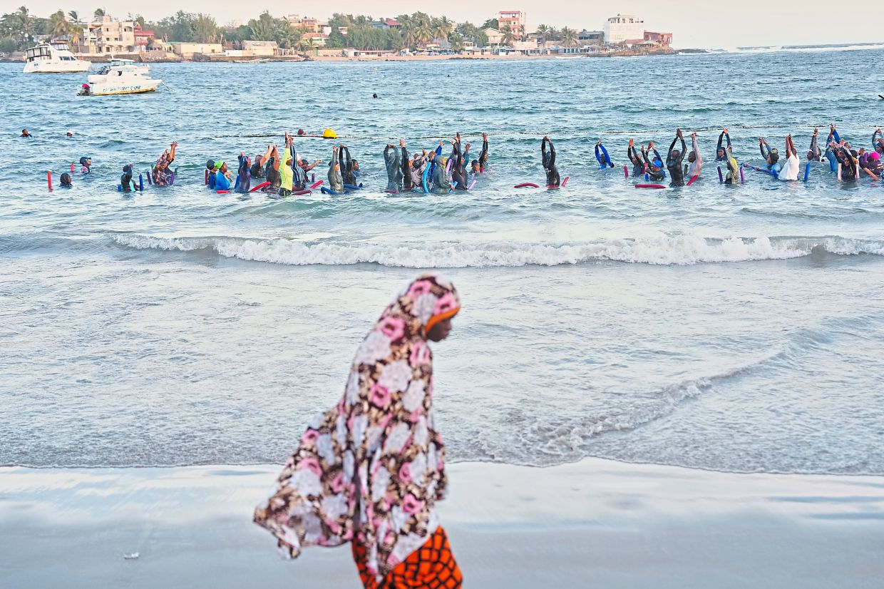 A lady walking on a beach as people take part in a group aquatic therapy session in Dakar. — AP