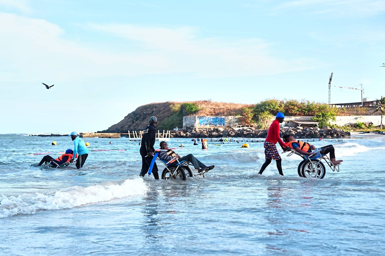Instructors assisting participants with limited mobility into the ocean for an aquatic therapy session. — AP