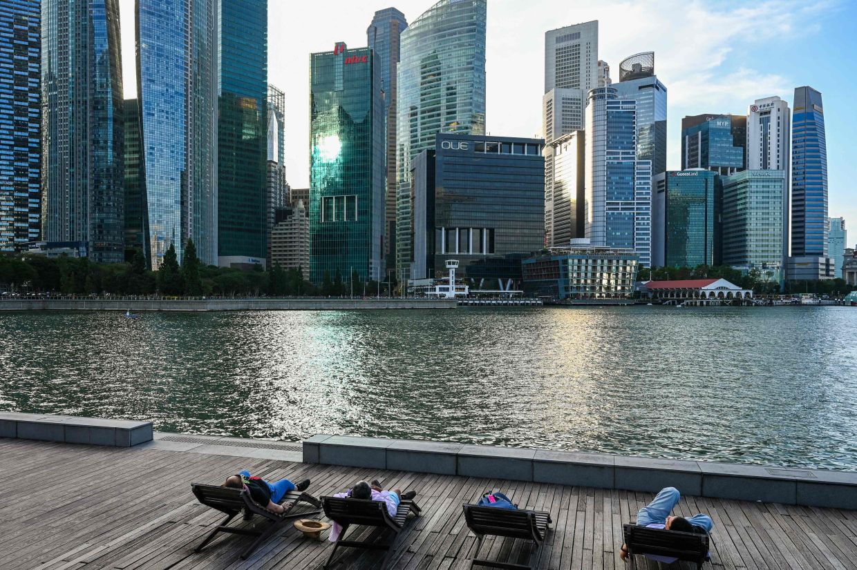 People relax on beach chairs along the boardwalk during sunset at Marina Bay in Singapore. -- Photo by Roslan RAHMAN / AFP