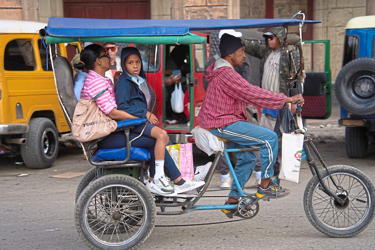 People riding a bicycle taxi in Havana. — AP 
