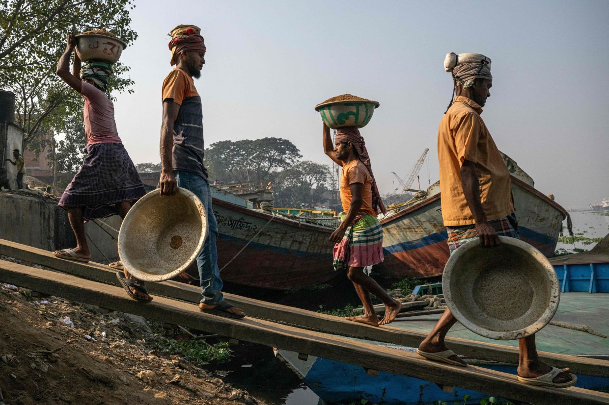 Bangladeshi men unloading buckets of sand on their heads from a cargo ship along the shore of the Buriganga River in Dhaka. National reconciliation must proceed on two tracks: political and economic. — AFP