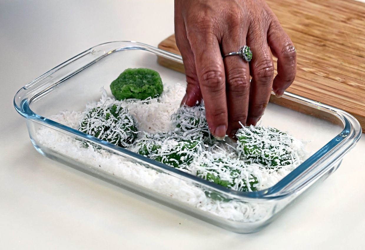 Coat the round glutinous ‘kuih lopes’ with grated coconut.
