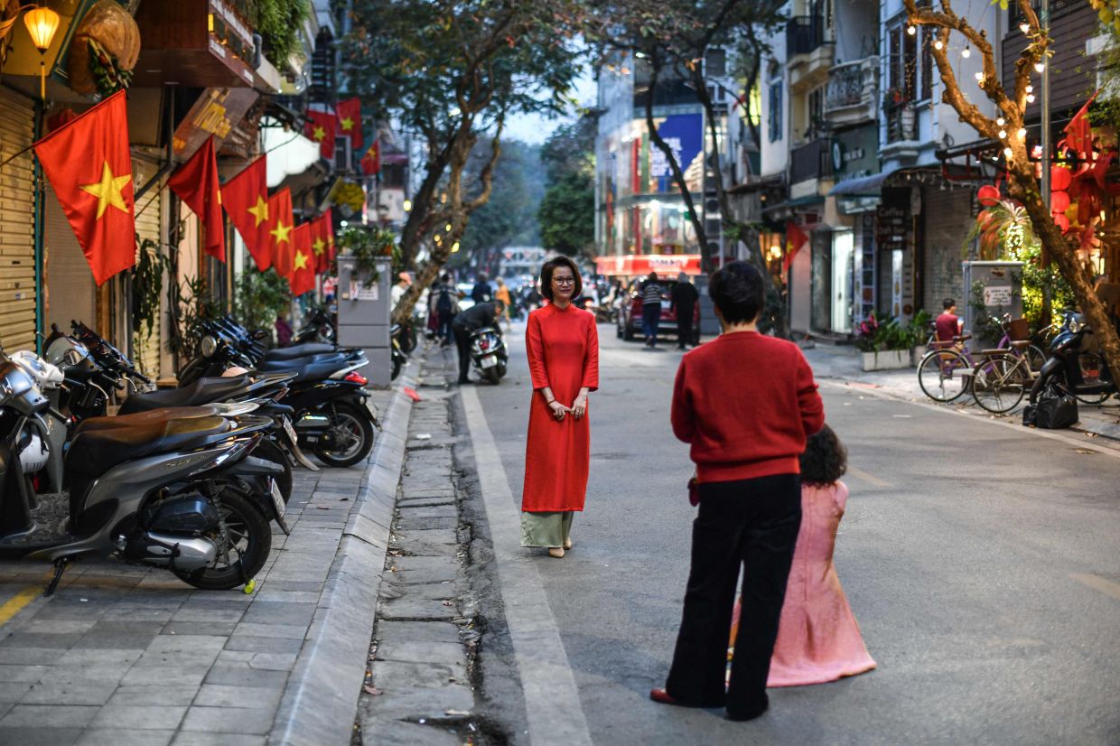 A woman poses for photos on a street near national flags during the Lunar New Year celebrations, known as Tet in Vietnam, in Hanoi. -- Photo by Amaury PAUL / AFP