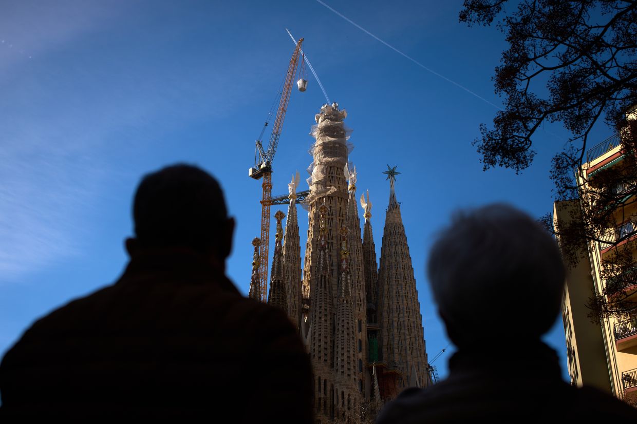 People watch as a crane lifts the upper arm of the cross onto the Tower of Jesus Christ at the Sagrada Familia in Barcelona on Feb 20, reaching the basilica's maximum height of 172.5m. Photo: AP