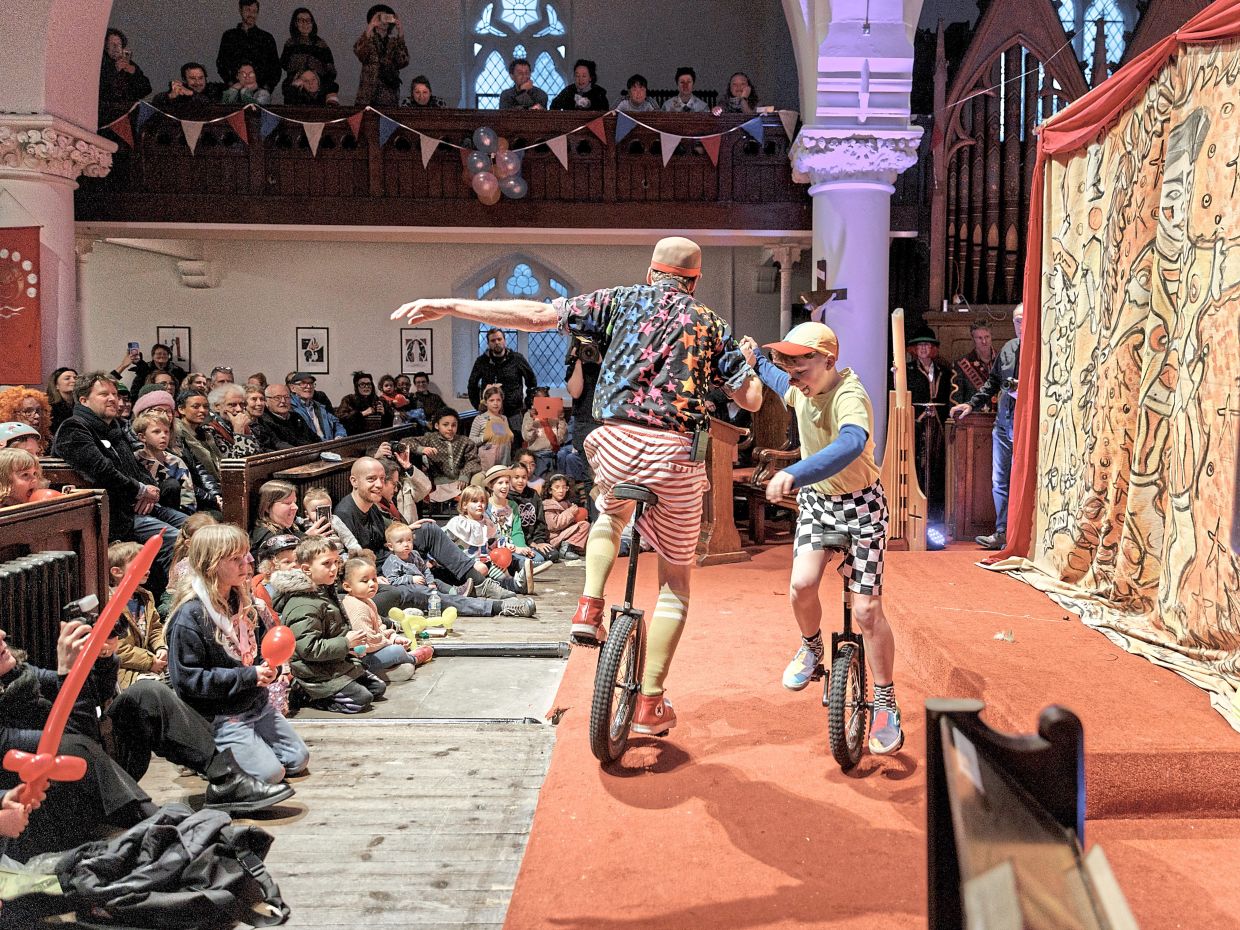 Ollie (right), the youngest clown in the church, rides a unicycle with his father, Clown Zaz, after a service honouring Grimaldi at All Saints Church.