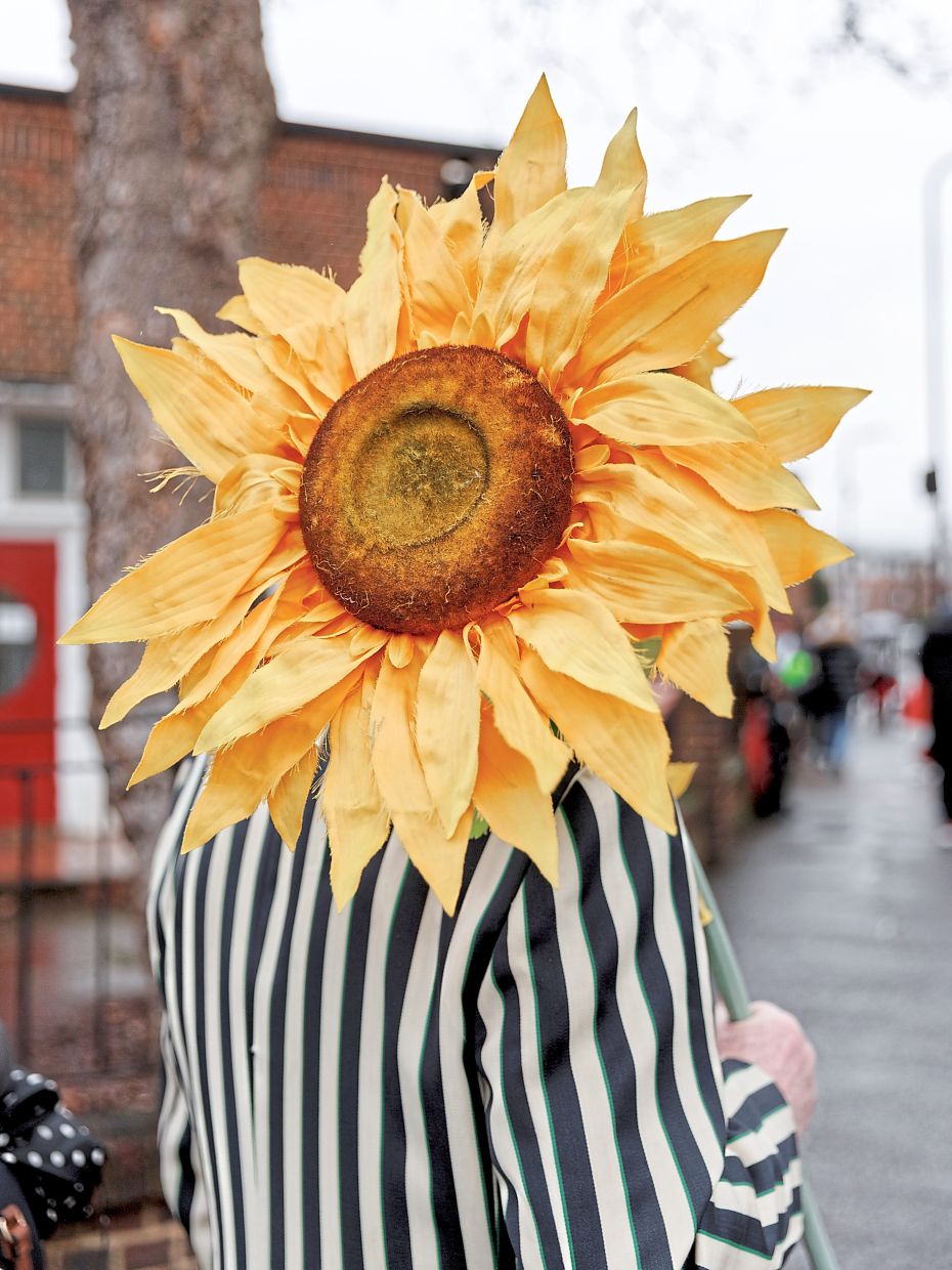 A clown holds a giant sunflower outside All Saints Church.