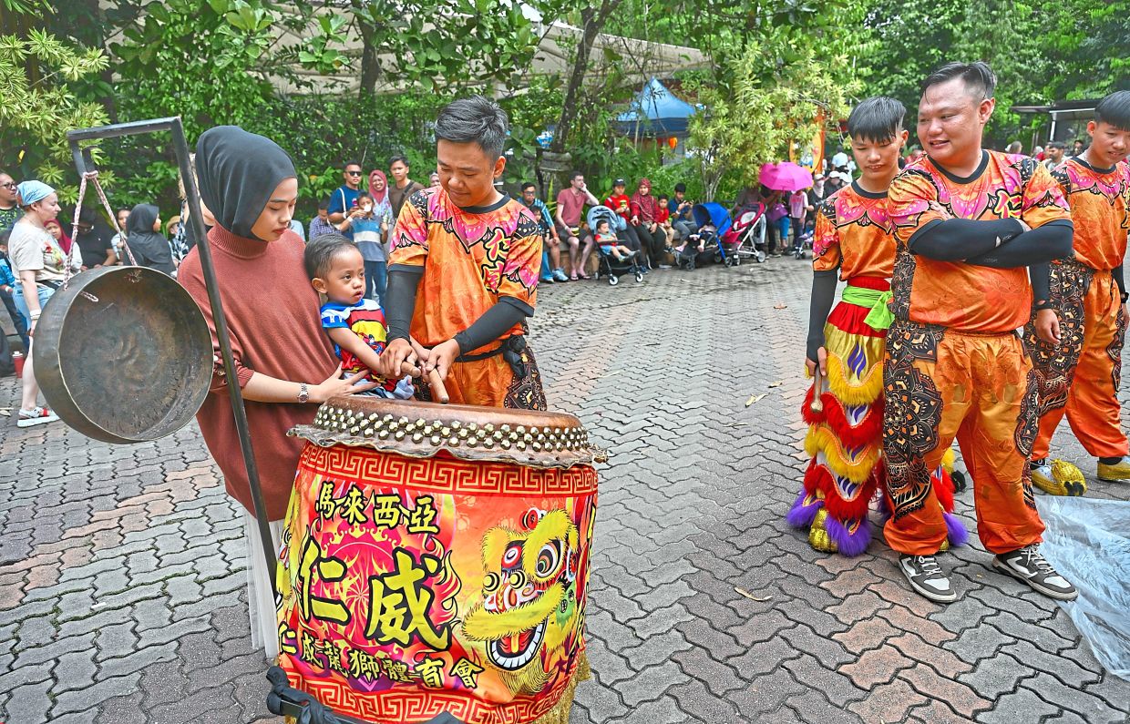 (From left) Arisha Syazwani Rahman and her two-year-old son Emir Zhafran Hakim trying their hand at drumming, with the assistance of a lion dance troupe member. 