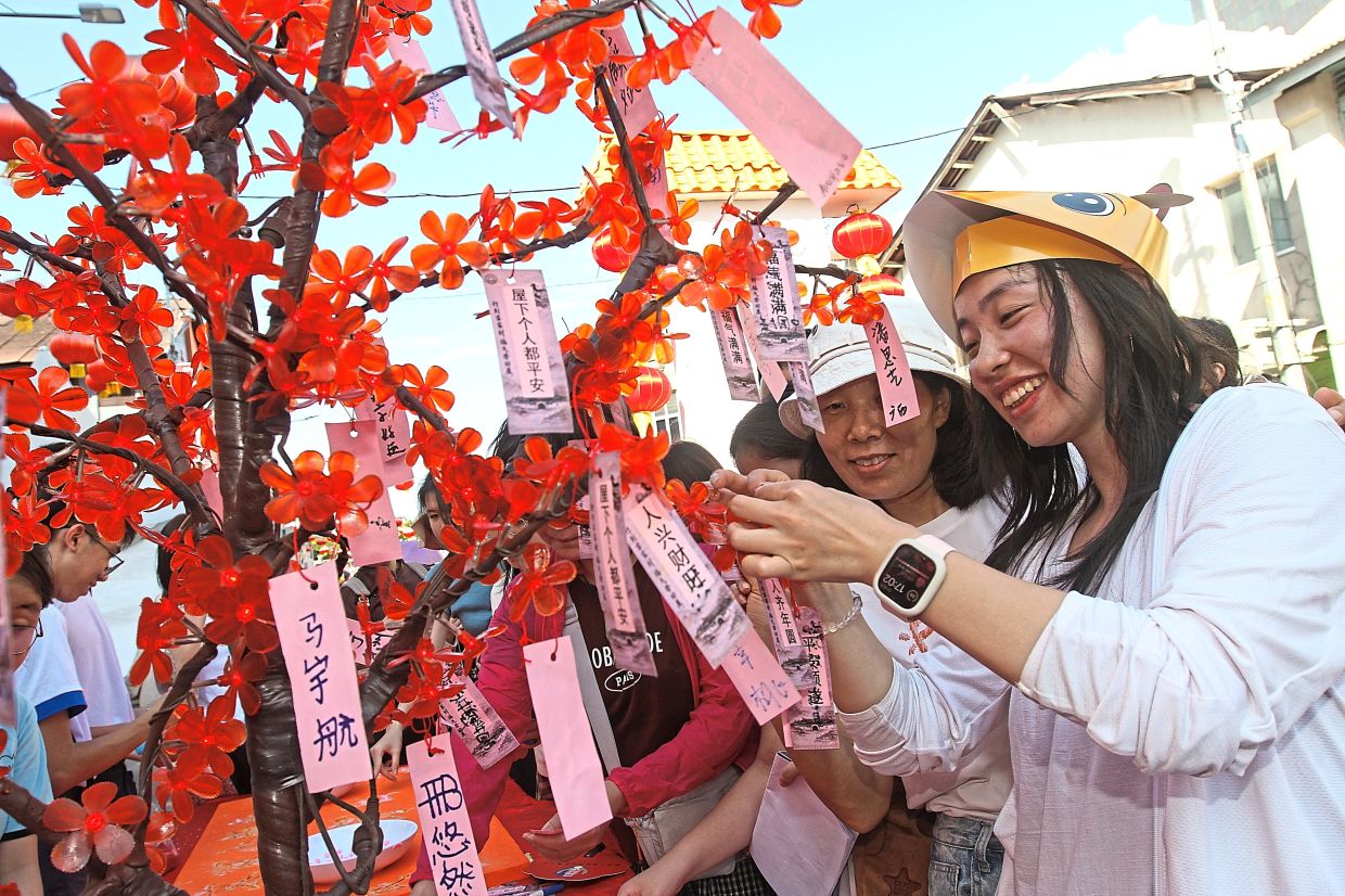 Chinese tourist Wang (right) and her mother Qi Cuiling hanging up blessings on a tree.