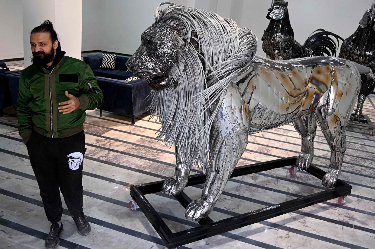 Sculptor Ehtisham Jadoon standing next to his creation made from scrap metal, a lion with a mane of twisted steel, at his studio on the outskirts of Islamabad. — Photo: Farooq NAEEM / AFP