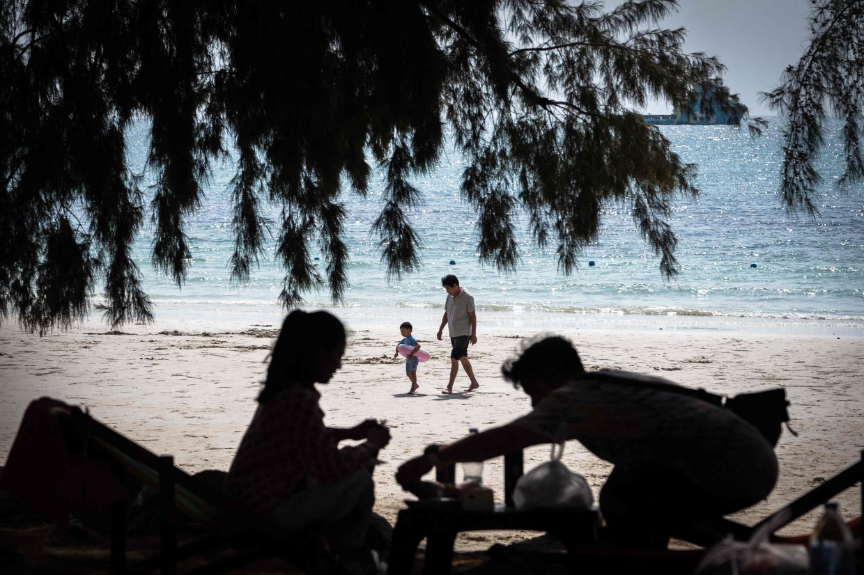 A man walks with a child with swimming gear along Nang Ram Beach in Pattaya on February 26, 2026. -- Photo by Chanakarn LAOSARAKHAM / AFP