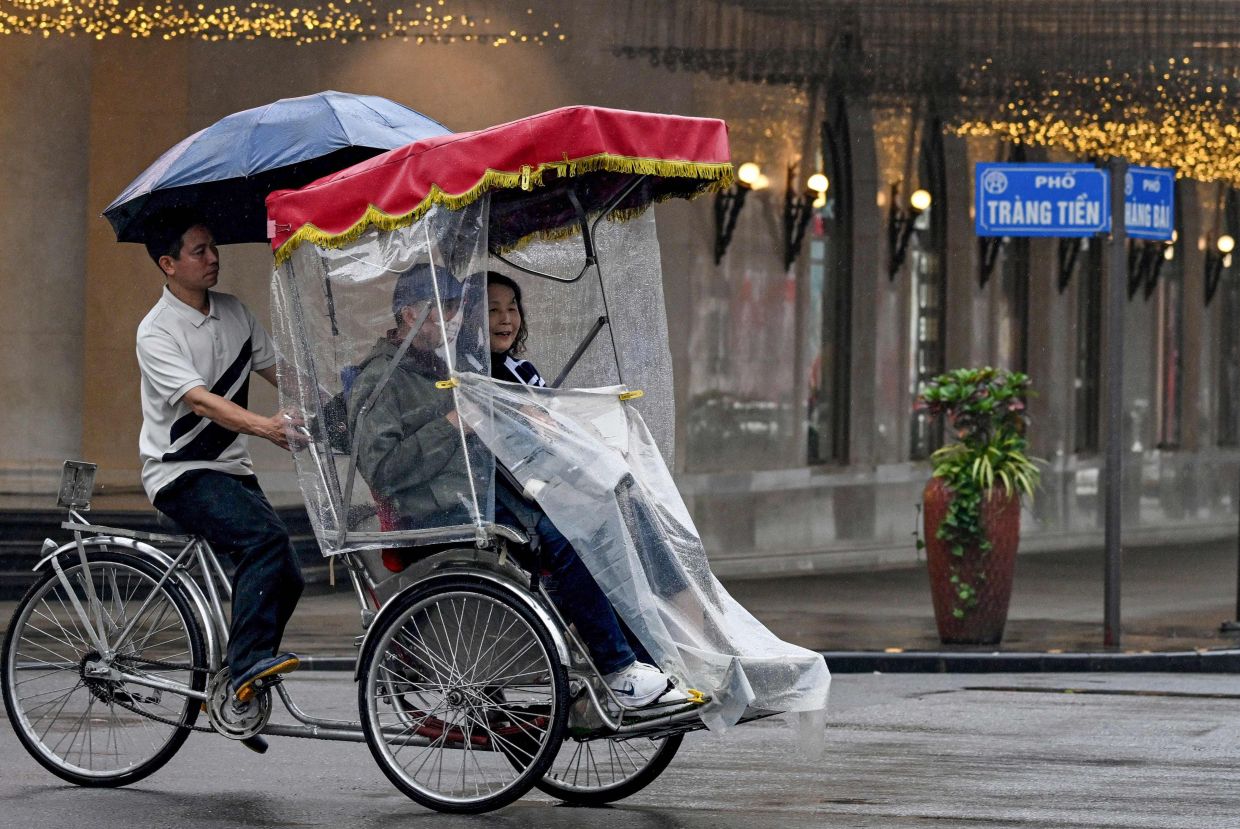 A cyclo driver ferries passengers through the rain in Hanoi. -- Photo by Nhac NGUYEN / AFP
